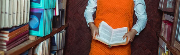 穿着橙色连衣裙的妇女拿着书 躺在图书馆地板上的全景照片 — 图库照片