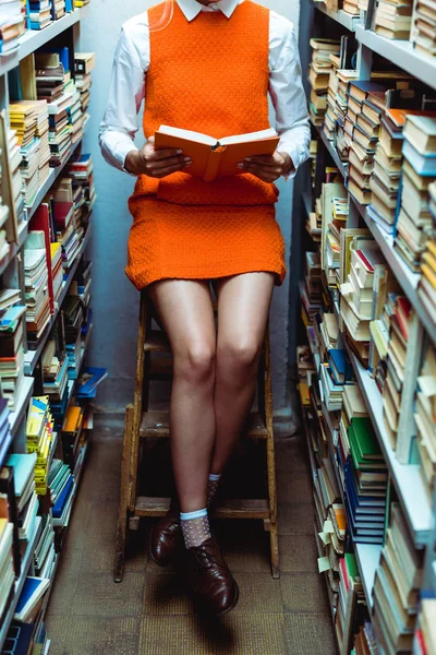 身着橙色连衣裙的女士在图书馆的梯子上坐视 — 图库照片