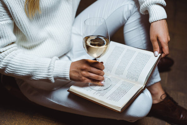cropped view of woman holding wine glass and book in library 