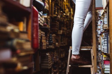 selective focus of woman standing on wooden ladder in library  clipart