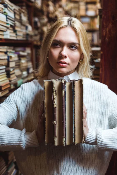 sarışın ve güzel kadın kitap tutan ve kütüphanede uzağa bakıyor 