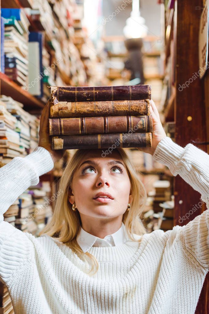 blonde and pretty woman holding books and looking up in library 