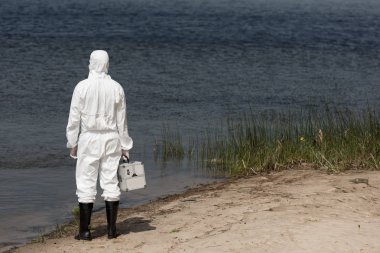 denetim kiti tutan ve nehir kıyısında duran koruyucu takım elbise su denetçisi geri görünümü