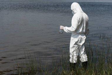 water inspector in protective costume holding flask while standing near river clipart