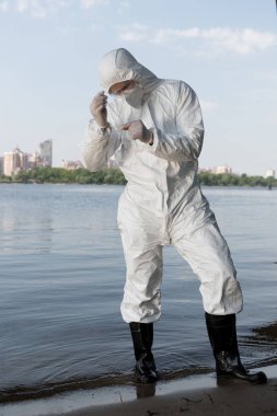 full length view of water inspector in protective costume and latex gloves taking water sample clipart