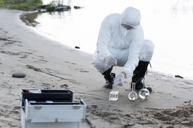 water inspector in protective costume and respirator taking water samples at river clipart