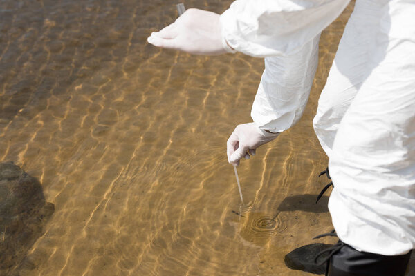partial view of water inspector in latex gloves with test tube taking water sample