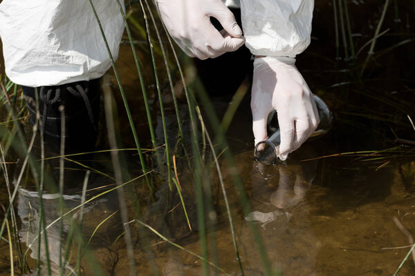 partial view of water inspector in latex gloves with flask taking water sample
