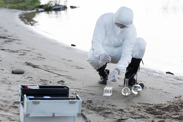 water inspector in protective costume and respirator taking water samples at river