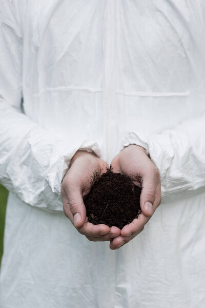partial view of ecologist in protective costume holding handful of soil
