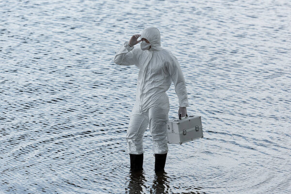 water inspector in protective costume holding inspection kit in river