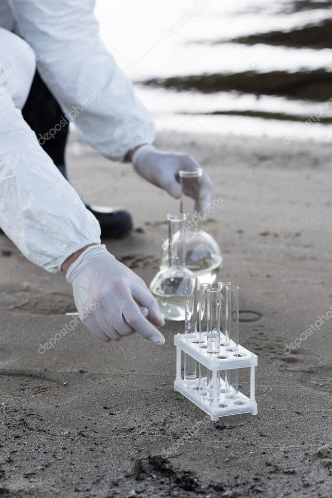 cropped view of water inspector in latex gloves with test tubes and flasks at coast