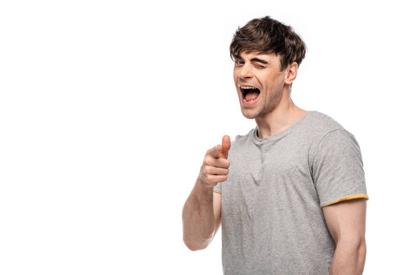 cheerful young man pointing with finger and winking at camera isolated on white