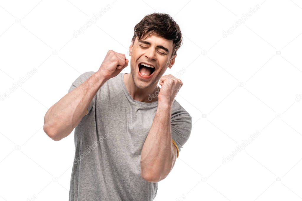 excited young man showing winner gesture with closed eyes isolated on white