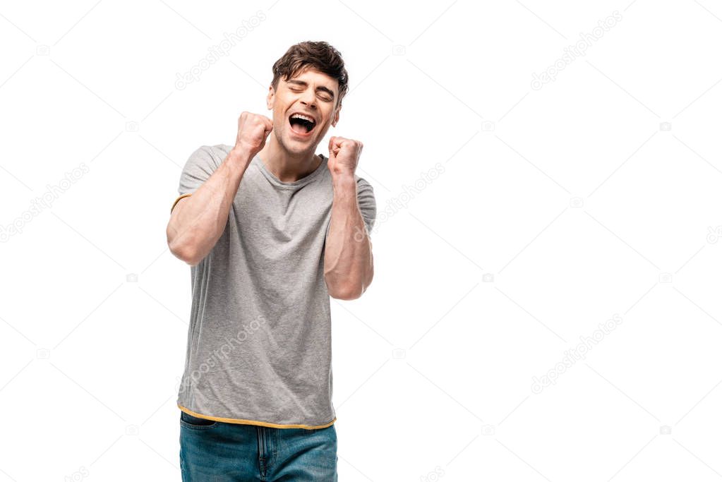 happy young man showing winner gesture with closed eyes isolated on white
