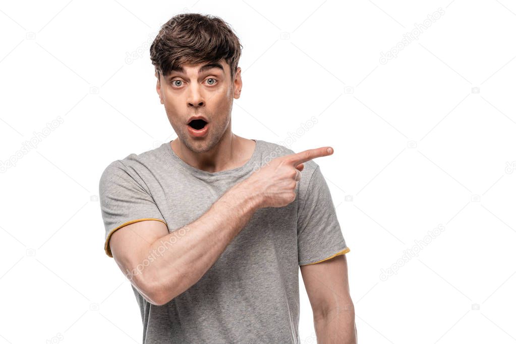 shocked young man pointing with finger and looking at camera isolated on white