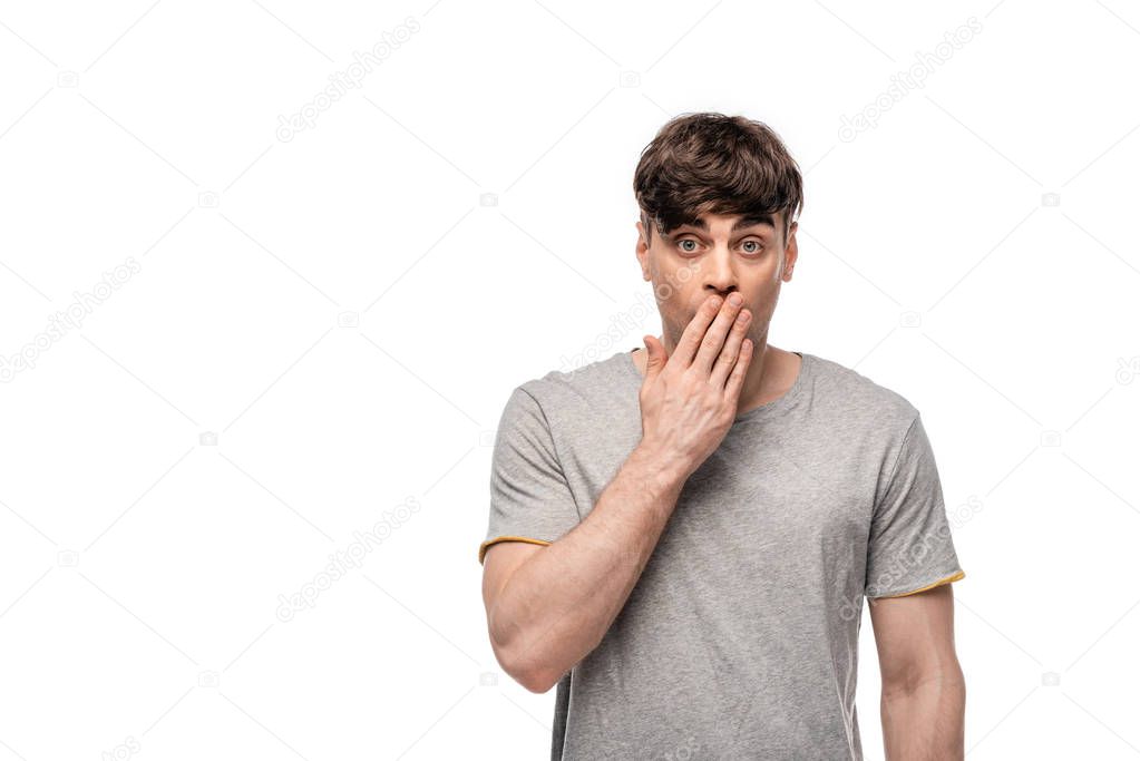 shocked young man looking at camera while covering mouth with hand isolated on white