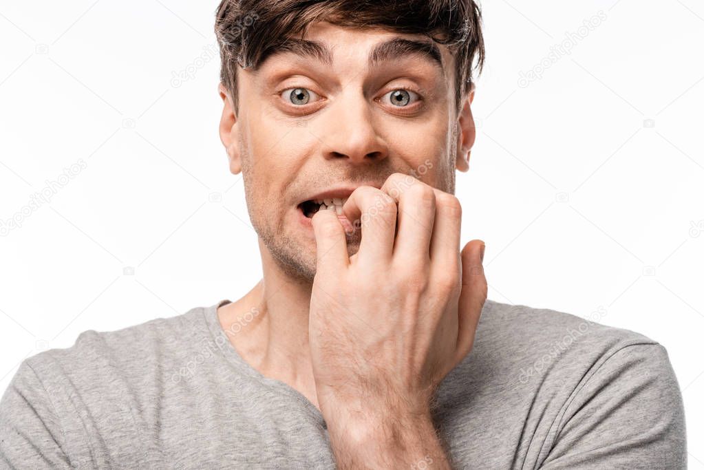 shocked young man looking at camera while holding hand near face isolated on white