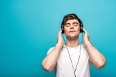 verträumter junger Mann mit Kopfhörern, der mit geschlossenen Augen auf blauem Hintergrund Musik hört