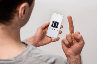 Kiev, Ukrayna - 16 Mayıs 2019: uber uygulaması ile akıllı telefon kullanan ve orta parmağını gösteren, gri üzerinde izole edilmiş adamın kırpılmış görünümü