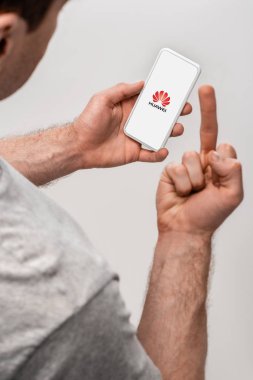 Kiev, Ukrayna - 16 Mayıs 2019: huawei uygulaması ile akıllı telefon kullanan ve orta parmağını gösteren, gri üzerinde izole edilmiş adamın kırpılmış görünümü