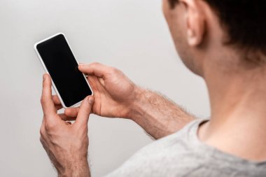 gri izole boş ekran ile akıllı telefon tutan genç adamın kırpılmış görünümü
