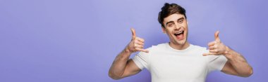 panoramic shot of cheerful man showing lets drink gestures and smiling at camera on blue background clipart