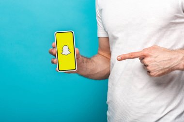 Kiev, Ukrayna - 16 Mayıs 2019: Snapchat uygulaması ile akıllı telefonu işaret eden adamın kırpılmış görünümü, mavi üzerine izole