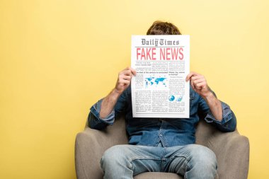 adam koltukta oturan ve sarı arka plan üzerinde sahte haber ile newspapaper okuma