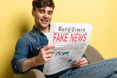 yakışıklı genç adam koltukta otururken gülümseyen ve sarı arka plan üzerinde iş gazetesi okurken