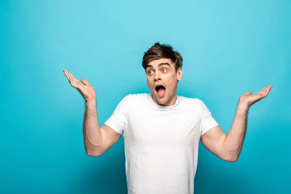 Discouraged Young Man Showing Shrug Gesture Looking Away Blue Background — Stock Photo, Image