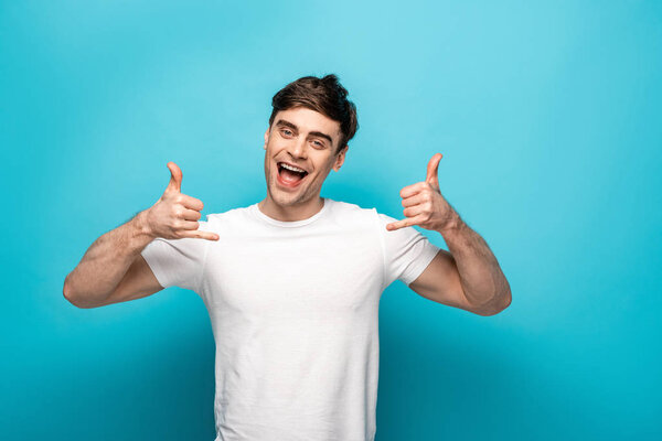 cheerful young man showing lets drink gestures while looking at camera on blue background