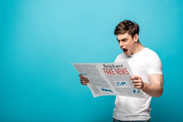 Сердитый Молодой Человек Читает Газету Фейковыми Новостями Синем Фоне — стоковое фото