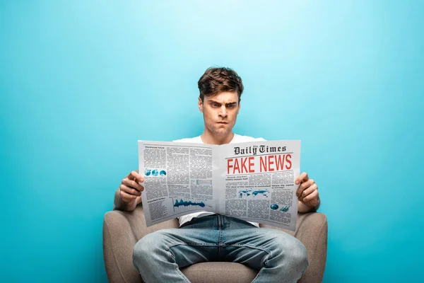 Сердитий Молодий Чоловік Читає Газету Фальшивими Новинами Сидячи Кріслі Синьому — стокове фото