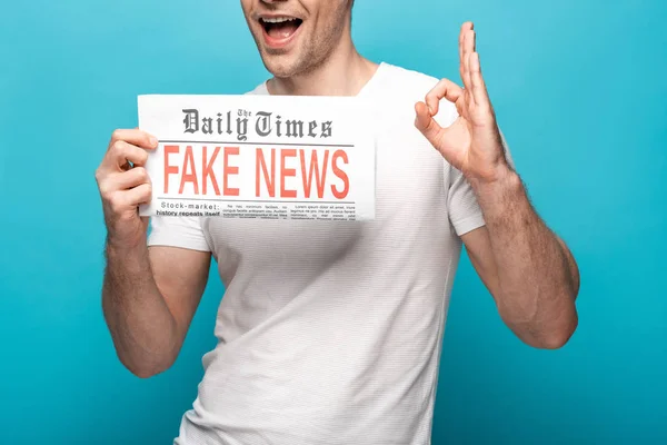 青い背景に偽のニュースで新聞を示しながらOk記号を示す男のトリミングビュー — ストック写真
