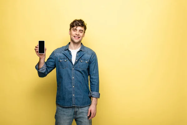 Красивый Молодой Человек Показывающий Смартфон Чистым Экраном Улыбающийся Камеру Желтом — стоковое фото