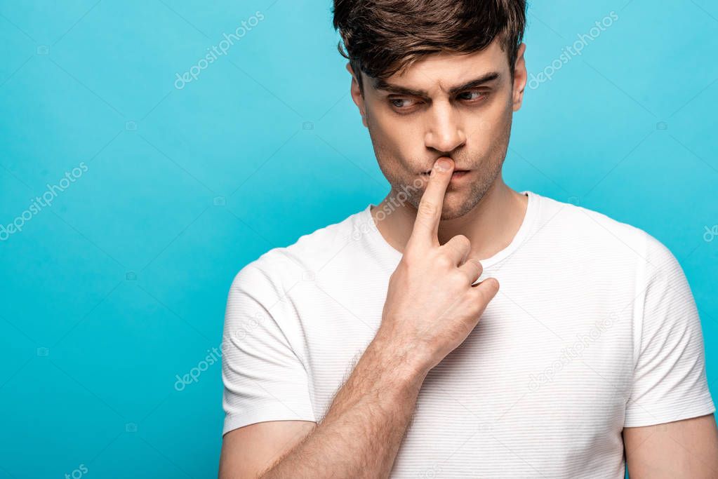 thoughtful man showing silence sign while looking away isolated on blue
