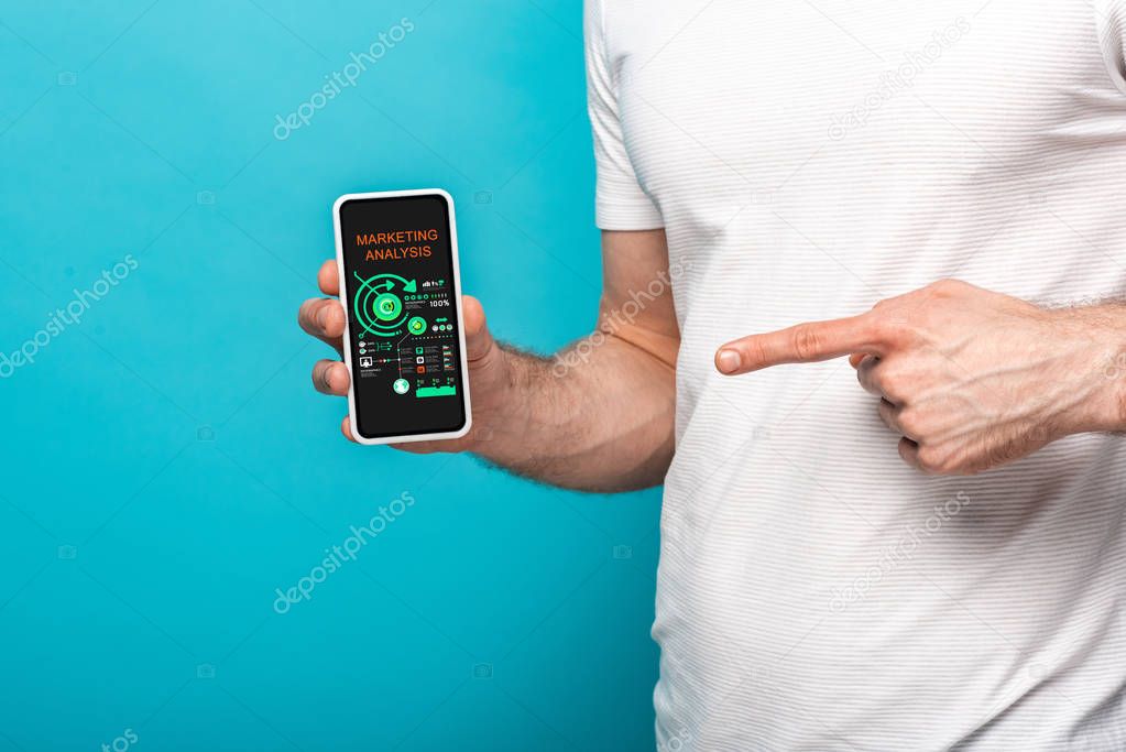 cropped view of man pointing at smartphone with marketing analysis app, isolated on blue