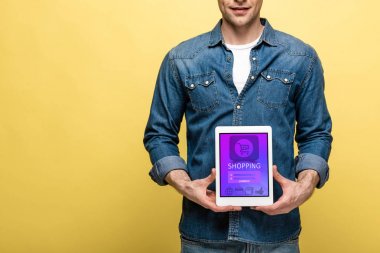 alışveriş uygulaması ile dijital tablet tutan denim giysiler içinde adam kırpılmış görünümü, sarı izole
