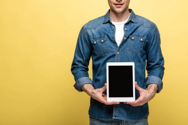 sarı arka plan üzerinde boş ekran ile dijital tablet tutan gülümseyen adam kırpılmış görünümü