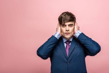 confident businessman covering ears wit hands isolated on pink clipart