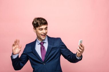 pembe izole akıllı telefon görüntülü sohbet sırasında el sallayarak gülümseyen işadamı