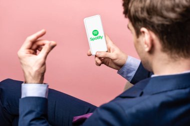 Kiev, Ukrayna - 16 Mayıs 2019: Spotify uygulaması ile akıllı telefon kullanan işadamının kırpılmış görünümü, pembe üzerinde izole