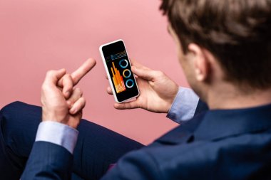 orta parmak gösterirken infografik ile akıllı telefon kullanarak işadamı kırpılmış görünümü, pembe izole