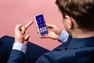orta parmak gösterirken sağlık uygulaması ile akıllı telefon kullanarak işadamı kırpılmış görünümü, pembe izole