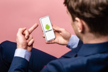 Kiev, Ukrayna - 16 Mayıs 2019: android uygulaması ile akıllı telefon kullanarak ve orta parmak gösteren işadamının kırpılmış görünümü, pembe izole