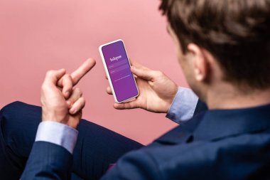 Kiev, Ukrayna - 16 Mayıs 2019: Instagram uygulaması ile akıllı telefon kullanan ve orta parmağını gösteren, pembe üzerinde izole edilmiş işadamının kırpılmış görünümü