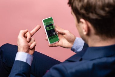 orta parmak gösterirken rezervasyon uygulaması ile akıllı telefon kullanarak işadamı kırpılmış görünümü, pembe izole