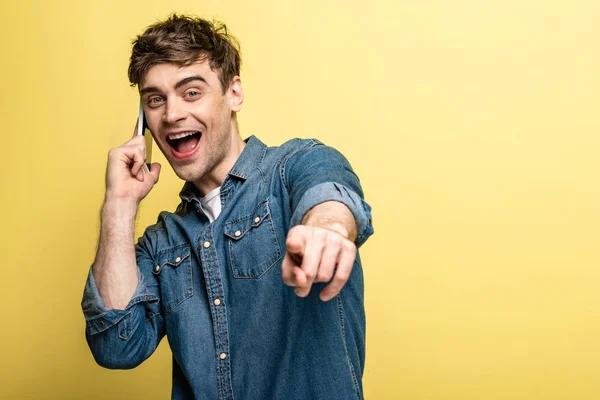 Excited Young Man Pointing Finger Camera While Talking Smartphone Yellow — Stock Photo, Image