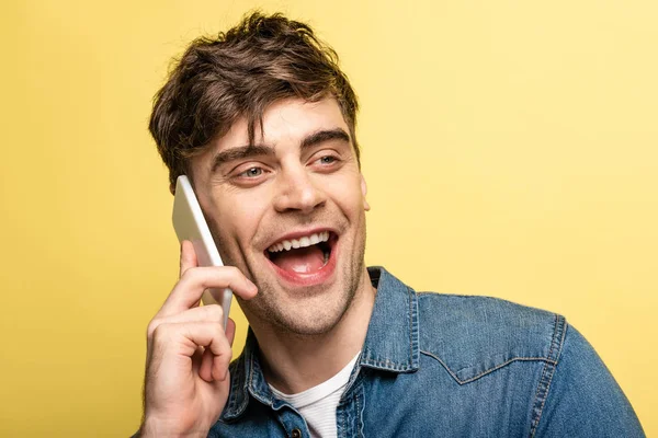 陽気な男は 黄色で隔離されたスマートフォンで話しながら 目をそらして笑う — ストック写真